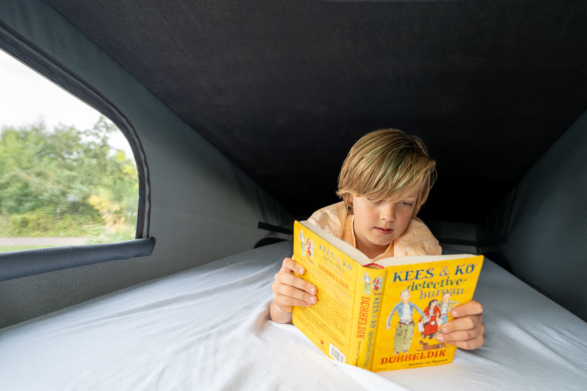 Kind leest een boek in het bovenbed van het hefdak